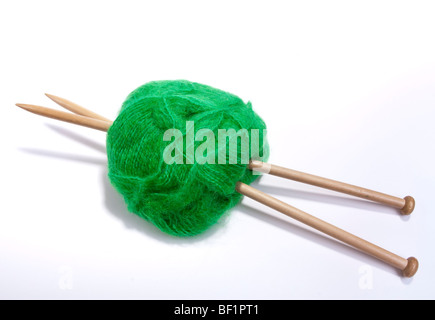 Large ball of green mohair wool or yarn pierced with large wooden knitting needles against white background. Stock Photo