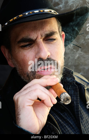 Man with beard in cowboy hat smoking cigar Stock Photo