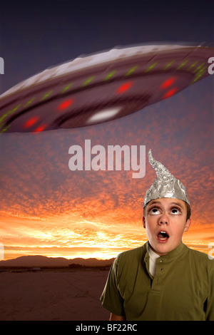 A bug-eyed boy, wearing a tin-foil hat observes a UFO in the sky.