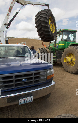 A tire technician works to change a tractor tire in the field during planting season / Pullman, Palouse Region, Washington, USA. Stock Photo