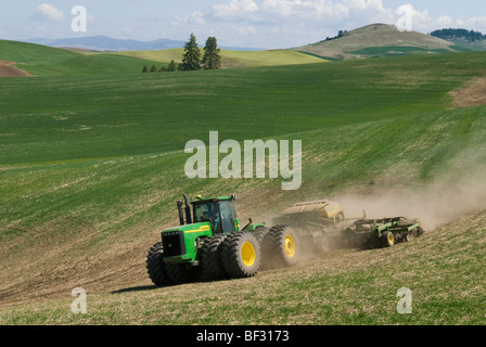 A tractor and air seeder replant areas of winter wheat damaged by lingering snow packs in the rolling hills of the Palouse / USA Stock Photo