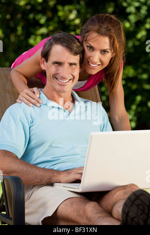 Happy attractive successful middle aged man & woman couple in their thirties, sitting together outside using a laptop computer. Stock Photo