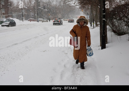 An elderly woman walks through walks slowly along a snow bound Montreal suburban street after a heavy snow storm. Stock Photo