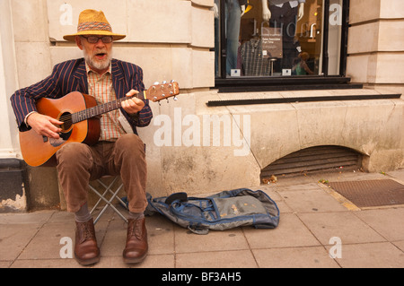 An elderly bearded man busker playing his guitar busking in Norwich , Norfolk , Uk Stock Photo