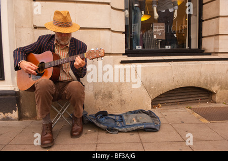 An elderly bearded man busker playing his guitar busking in Norwich , Norfolk , Uk Stock Photo