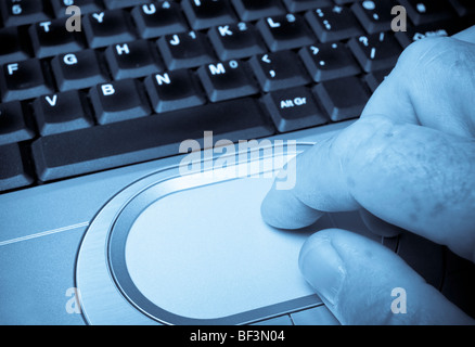 Blue toned monochromatic image of finger and laptop keyboard with shallow focus Stock Photo