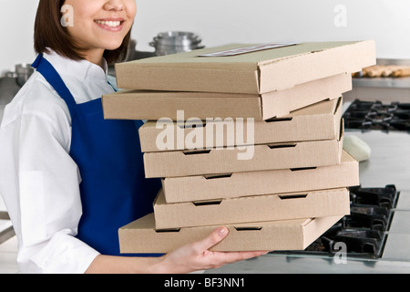 Female chef holding stack of pizza boxes and smiling Stock Photo