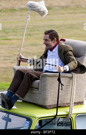 Rowan Atkinson, aka Mr Bean, rides an armchair on the roof of a Mini 1000 at Goodwood Revival meeting, Sussex, UK. Stock Photo