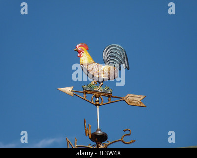 A decorative metal weather vane in the shape of a brightly coloured cockerel, with a pointing arrow, against a bright blue sky Stock Photo