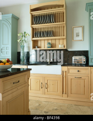 Pale wood plate-rack and granite splash-back above Belfast sink in fitted wood unit in pale blue country kitchen Stock Photo