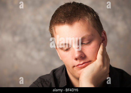Young man thinking with a pensive bored expression resting chin on hand. UK, Britain. Stock Photo