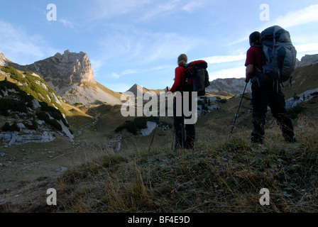Hikers, young man and woman walking with backpacks and trekking poles towards Mt. Rosskopf, 2257 m, through the still frost-cov Stock Photo