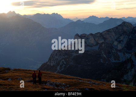 Young man and woman, hikers, looking down from Mt. Heidachstellwand, 2192m, in the sunset, towards the Karwendel mountain range Stock Photo