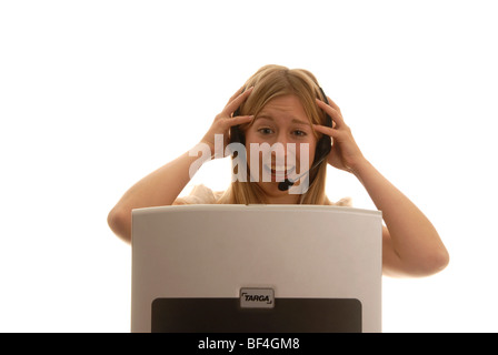 Eighteen year old woman behind a laptop with a headset, laughing, tearing her hair Stock Photo