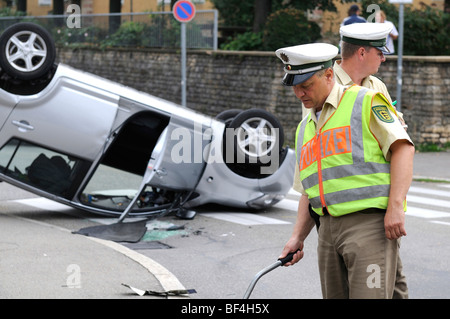 Daihatsu car having rolled over in a traffic accident, lying on its roof, police officer writing up the accident, surveying, St Stock Photo