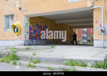 Man walking through abandoned apartment building entrance with graffiti on wall, Russia Stock Photo