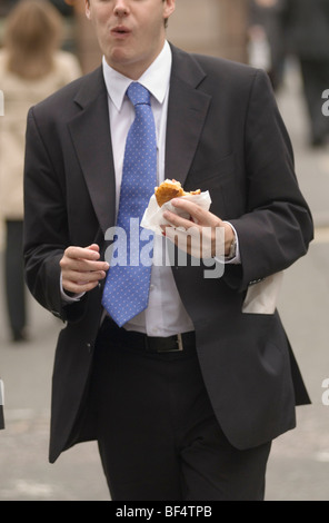Man eating hamburger in street walking back to his office London city office worker. UK 2009 2000s HOMER SYKES Stock Photo