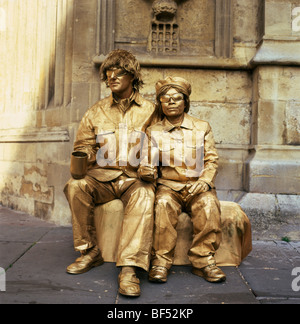 Gold painted street entertainer entertainers living statues with coin collection cups near Bath Cathedral, Bath, England UK Great Britain KATHY DEWITT Stock Photo