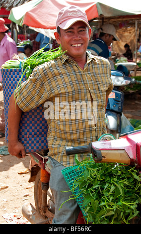 Man carrying baskets of vegetables on a motorcycle to sell at the market in Skuon, Cambodia Stock Photo