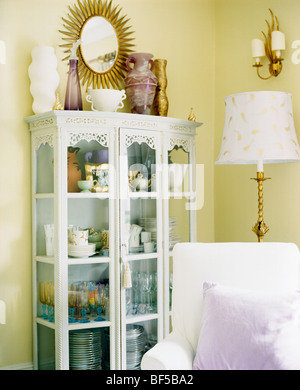 Vases on top of white painted glass-front cupboard in pastel yellow living room with white armchair Stock Photo