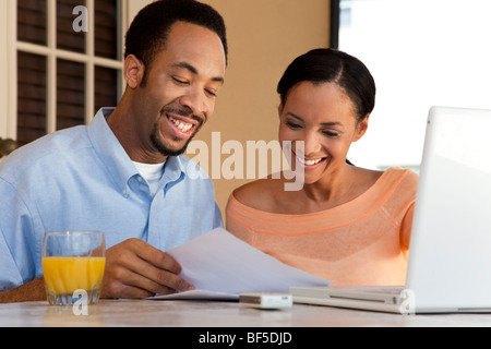 A happy African American man and woman couple in their thirties working on a laptop computer and looking at paperwork Stock Photo