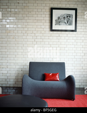 Red cushion on modern grey armchair against white ceramic brick wall in modern living room Stock Photo
