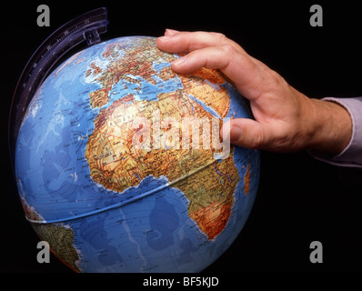 Close up male hand on world globe concept image getting a grip on wider view of worldwide affairs such as in the African Continent a studio shot in UK Stock Photo