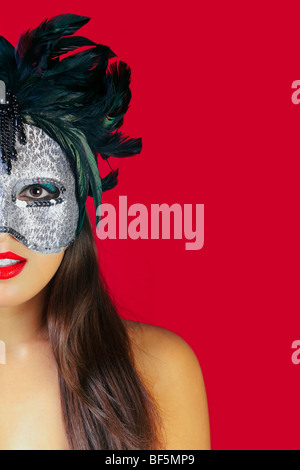 Beautiful brunette woman wearing a masqurade mask against a red background. Stock Photo