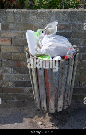 street rubbish bin overflowing with garbage attached to brick wall Stock Photo