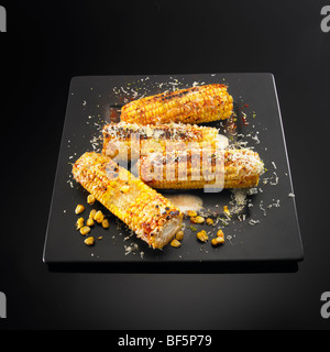 Barbecued corn cobs with cheese, butter and chili, on a black background. Stock Photo