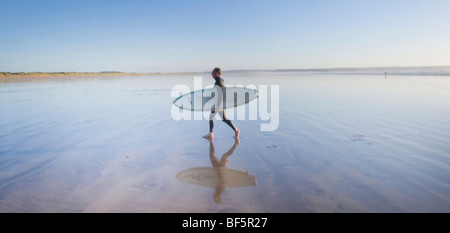 A surfer walks along the beach reflected in the wet sand on the north devon coastline