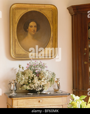 Close-up of gilt-framed portrait above flower arrangement on small chest-of-drawers Stock Photo