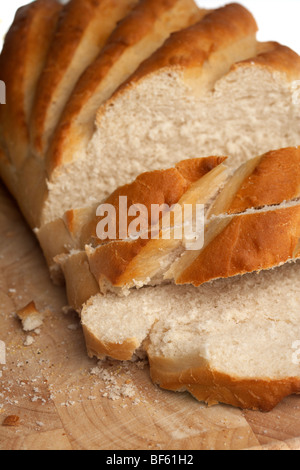 fresh white crusty bloomer loaf cut into rough slices on a wooden block Stock Photo