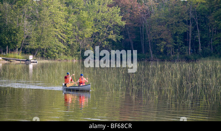 Morning Canoe Paddle. A couple, both wearing life vests, enjoys a morning paddle on a smooth but weedy small Quebec lake Stock Photo