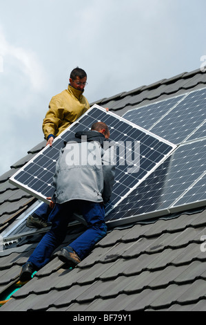 workmen installing photovoltaic solar panels on the roof of a private house Stock Photo