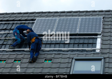 workmen installing photovoltaic solar panels on the roof of a private house Stock Photo