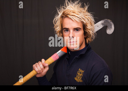 Head and shoulders portrait of a young man with a determined expression wearing a hockey shirt with a stick over his shoulder. UK Stock Photo