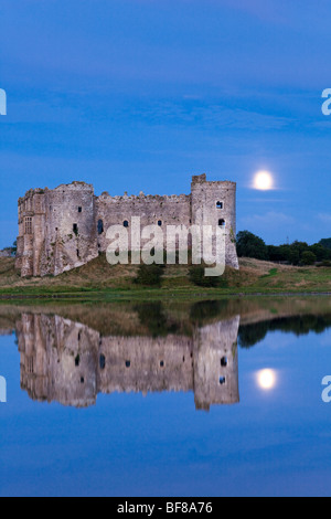 The moon rising behind Carew Castle beside the Carew River at Carew, Pembrokeshire, Wales UK Stock Photo