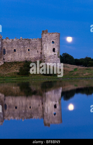 The moon rising behind Carew Castle beside the Carew River at Carew, Pembrokeshire, Wales UK Stock Photo