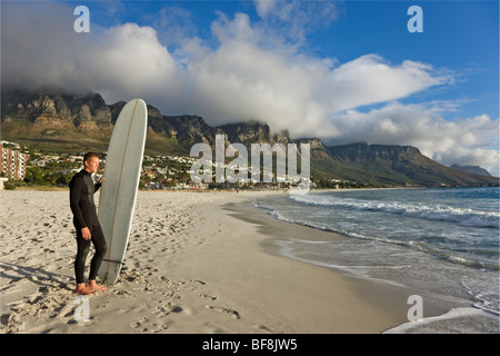 Surfer on camps bay beach with twelve apostles of Table Mountain in background. Cape Town South Africa Stock Photo
