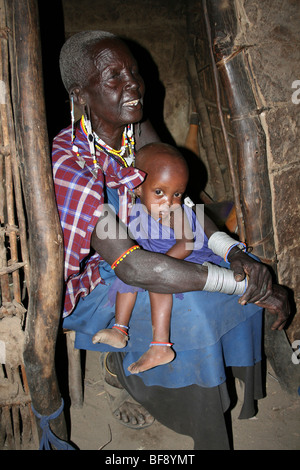 Elderly Masai Woman With Grandchild In Her Home In Engaruka Village, Rift Valley, Tanzania Stock Photo