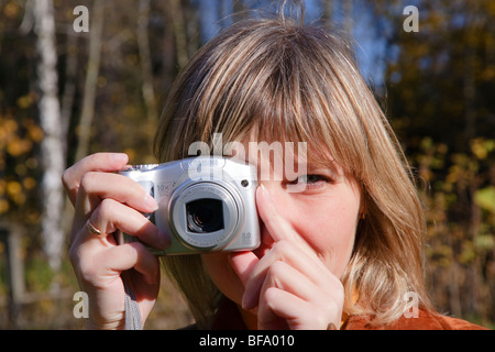 Young woman making photos using compact camera on autumn forest Stock Photo