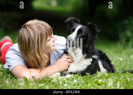 mixed breed dog (Canis lupus f. familiaris), trainer lying on the belly caressing a dog, Border Collie-Terrier-Mix, in a meadow Stock Photo