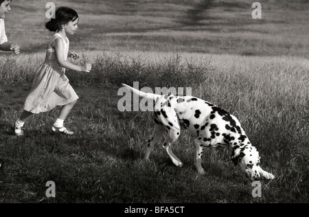A boy and a girl running over Primrose Hill with a Dalmation Dog. The dog has a smiling artful expression as in the cartoon Stock Photo