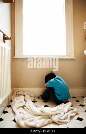 A upset boy sits on the floor of the bathroom with his back turned to camera Stock Photo