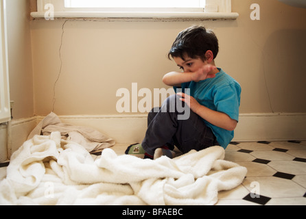 A upset boy sits on the floor of the bathroom and wipes his face Stock Photo