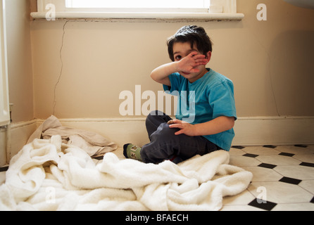 A upset boy sits on the floor of the bathroom and wipes his face Stock Photo