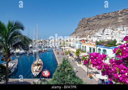 Puerto de Mogan view over bougainvillea flowers to yacht marina  promenade and restaurants  Gran Canaria Canary Islands Spain Stock Photo