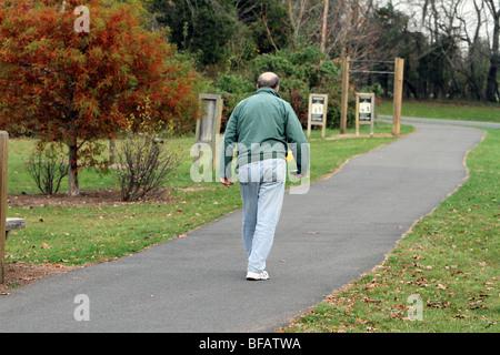 A senior bald headed man walking in the park for exercise. Shot in autumn trees have changed colour color Stock Photo