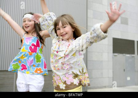 Two little girls dancing in the city with gray building in background Stock Photo